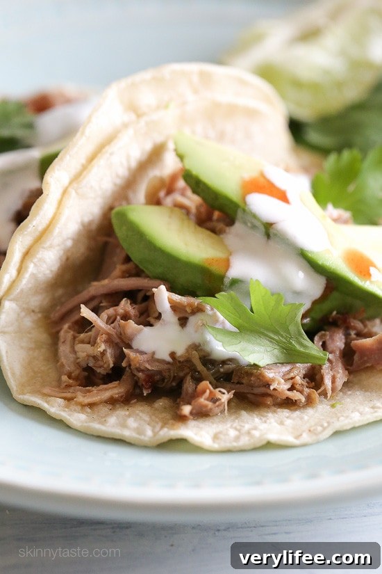Instant Pot carnitas tacos on a plate topped with avocado slices, cilantro, and cheese.