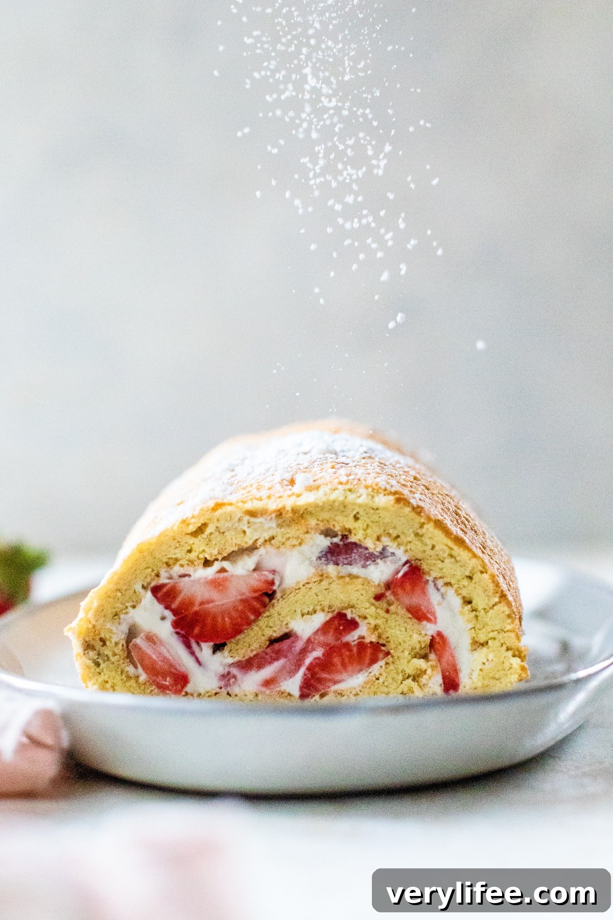 Strawberry Swiss Roll Recipe 9 Strawberry Swiss Roll on a plate, sliced in half.