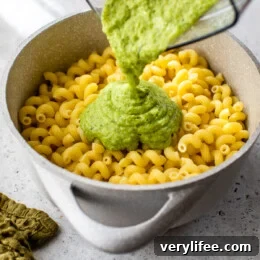 Creamy Zucchini Pasta Recipe 4 Creamy zucchini sauce being poured into a pot of cooked pasta.