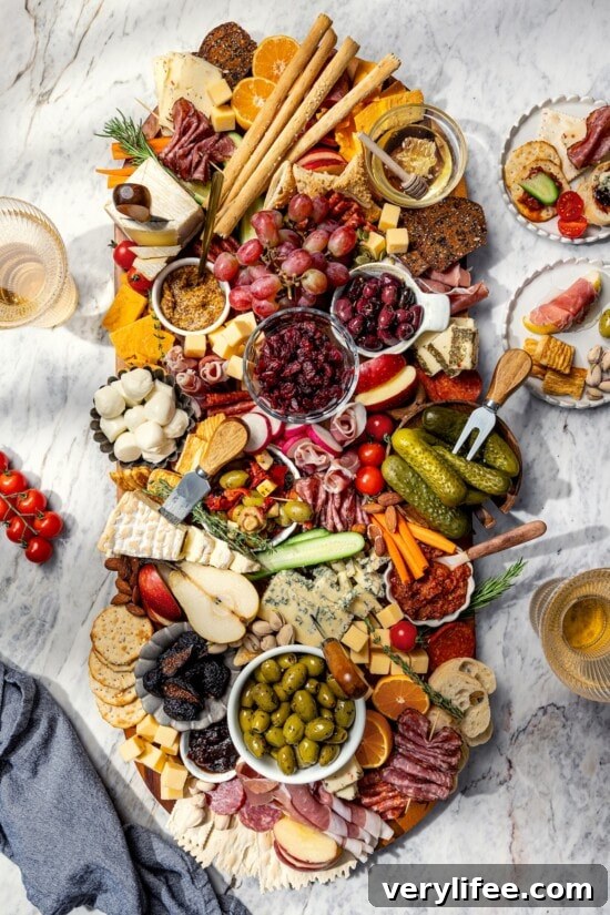 Plates surrounding large charcuterie and cheese board with fruit, pickles, olives, and spreads.