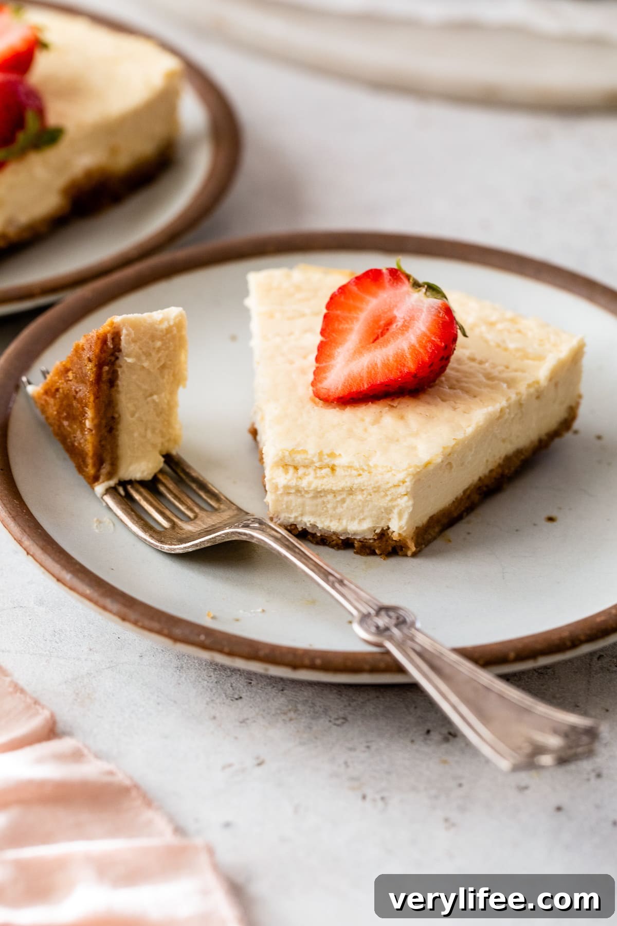 A slice of creamy cottage cheese cheesecake topped with a fresh strawberry on a plate, with a forkful missing from the end.