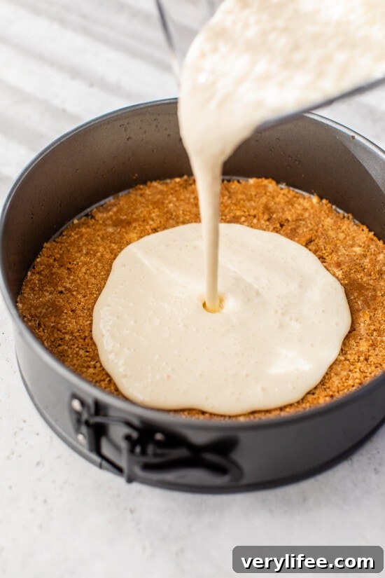 Pouring the cheesecake batter on top of a graham cracker crust in a springform pan.