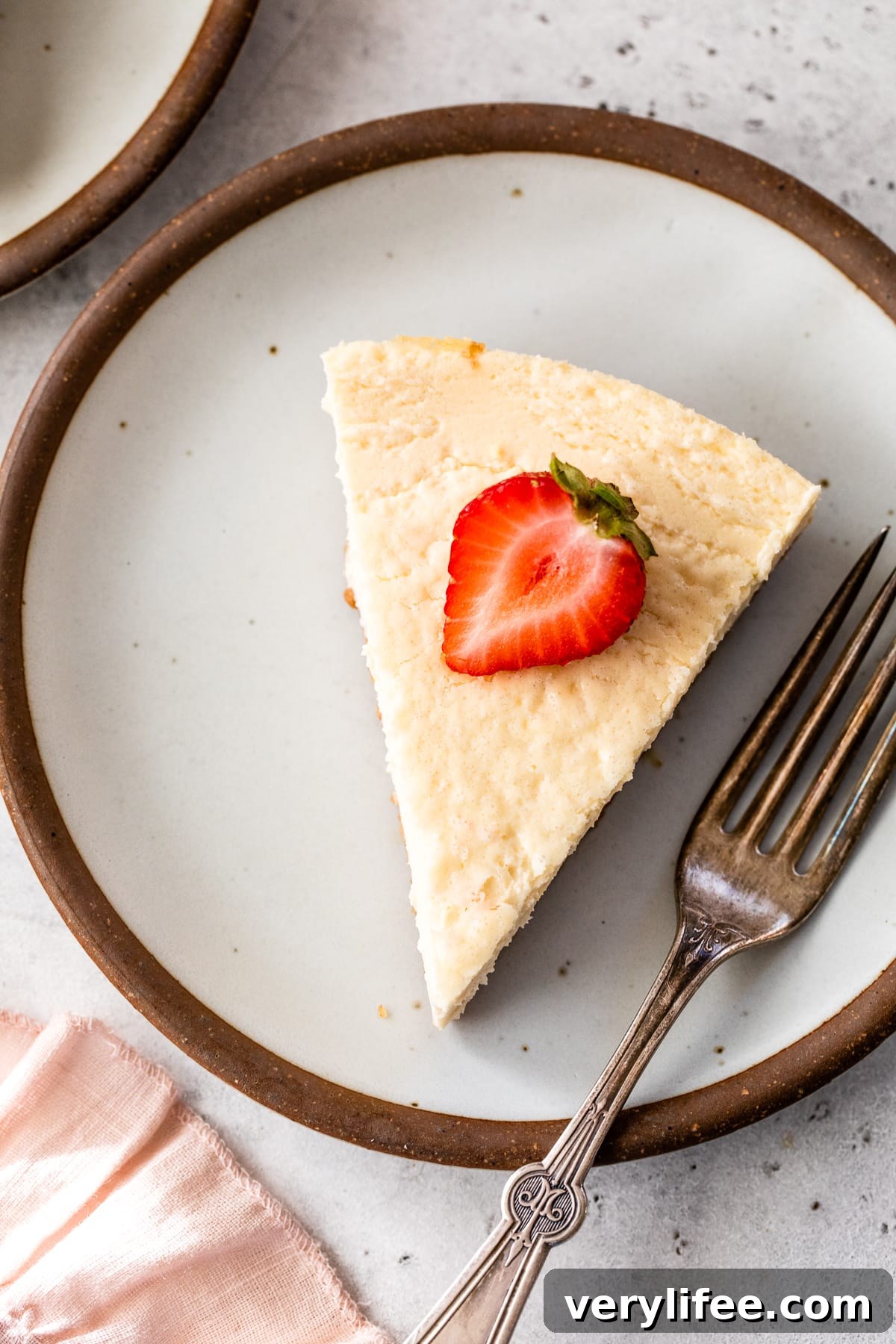 Overhead view of a slice of creamy New York-style cottage cheese cheesecake topped with a fresh strawberry on a plate.