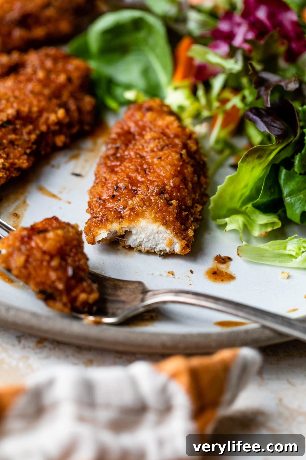 BBQ chicken tender being cut A fork cutting into a BBQ chicken tender next to green salad on a plate.