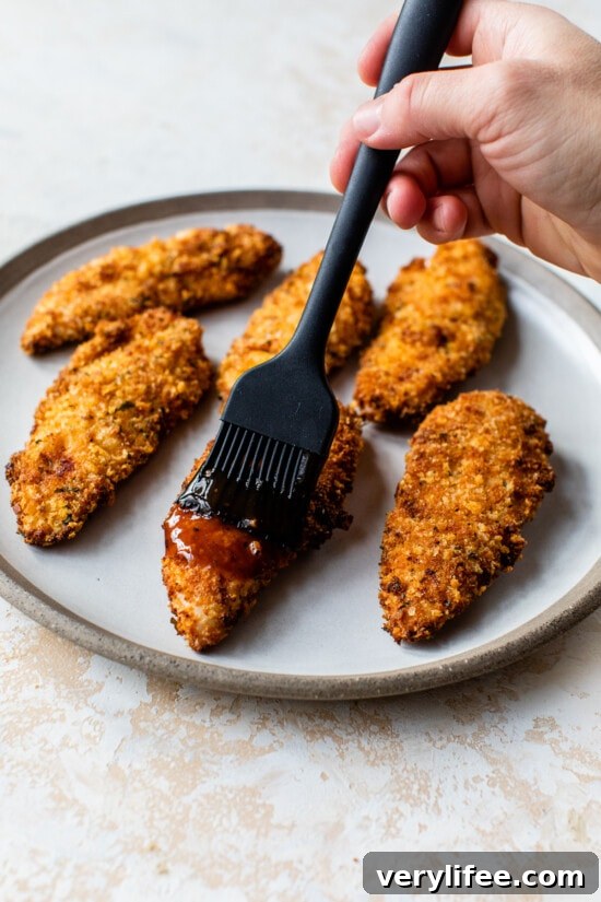 Brush with sauce Brushing BBQ sauce over air fried chicken tenders on a plate.