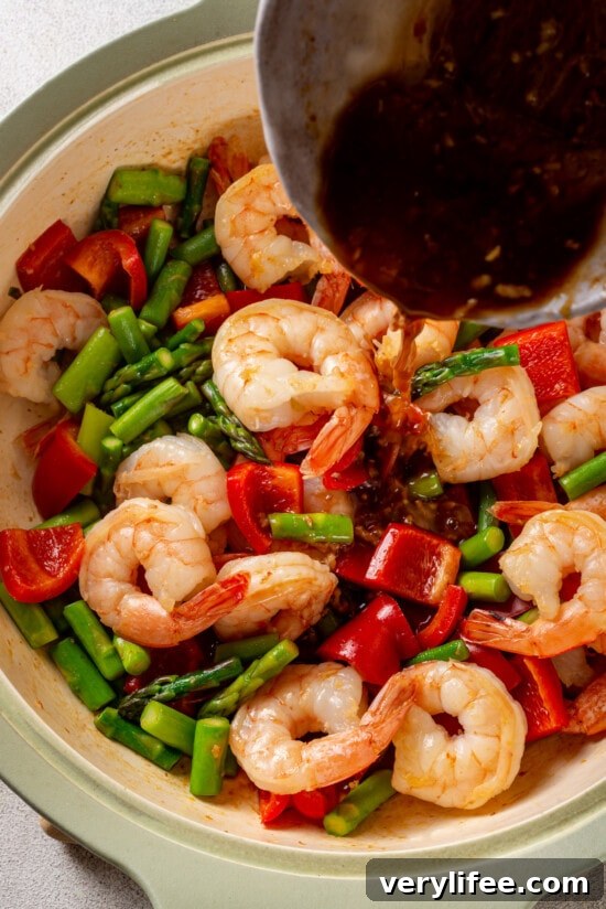 Stir fry sauce being poured over shrimp, asparagus, and red bell peppers
