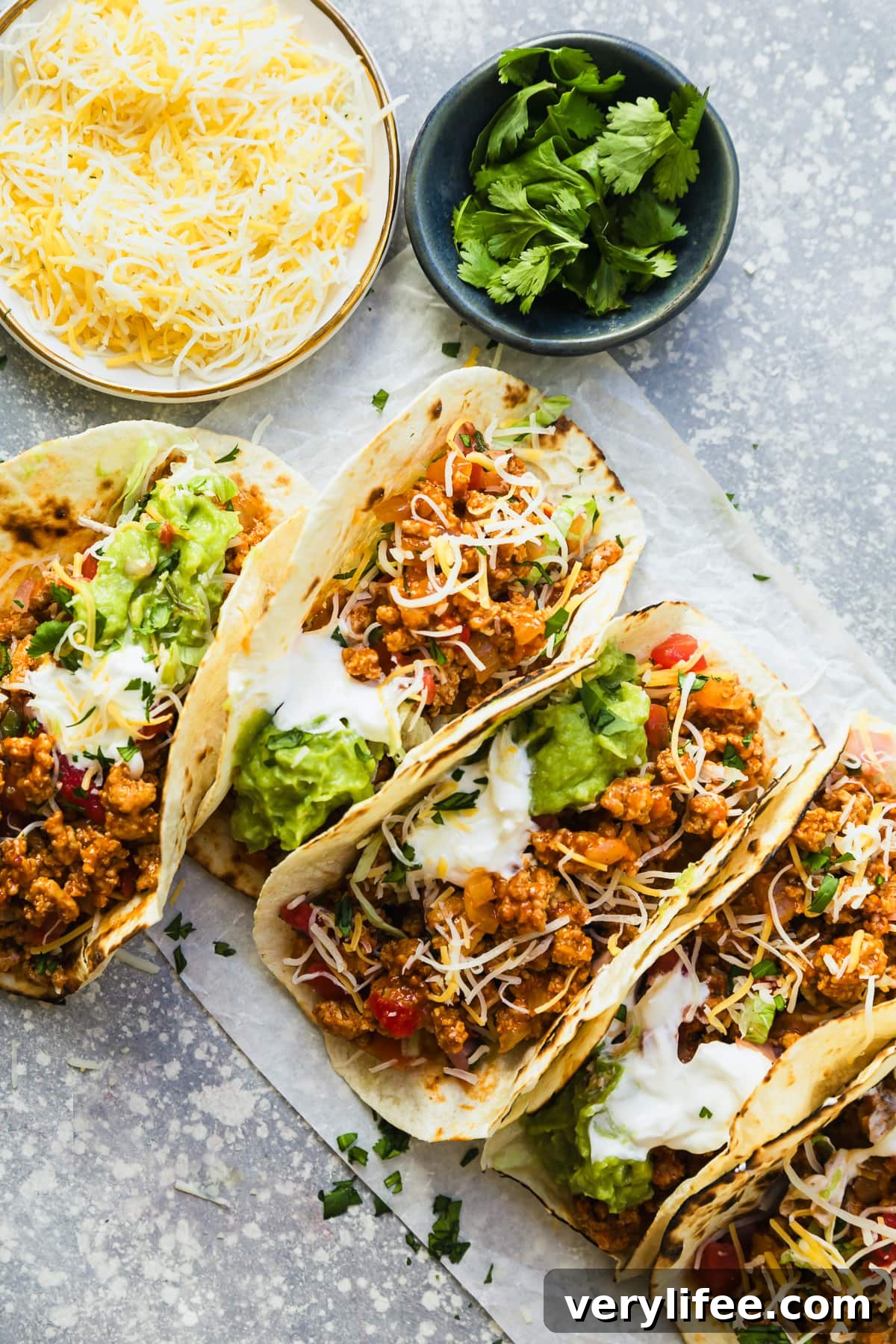 Savory Ground Turkey Tacos with Avocado Crema 8 Tacos on a table with cheese and cilantro