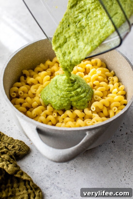 Creamy zucchini sauce being poured into a pot of cooked pasta.