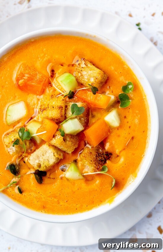 Overhead view of a bowl of gazpacho topped with fresh chopped cucumber, tomato, and crunchy croutons.