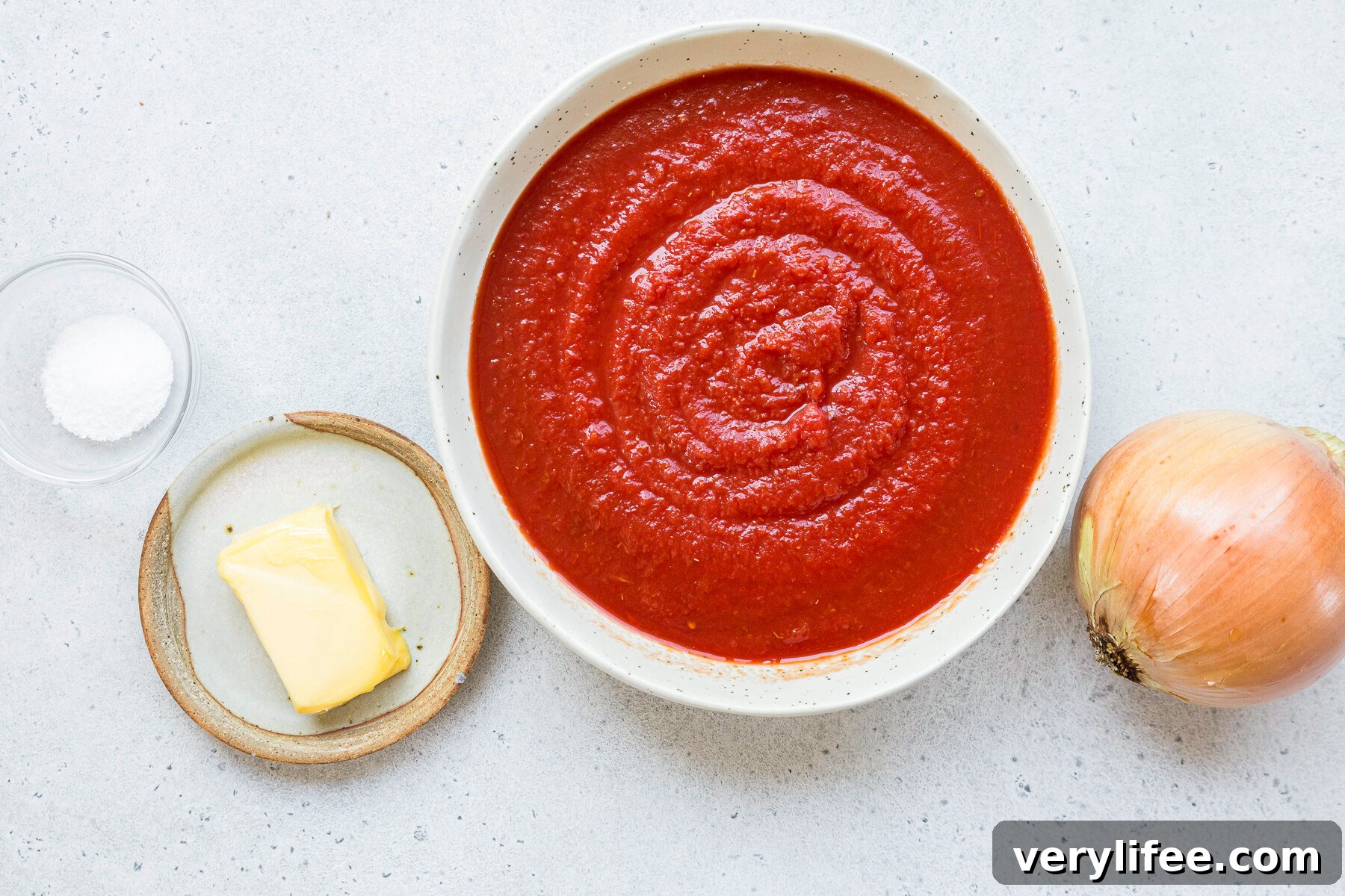 Ingredients for tomato sauce including canned tomatoes, butter, and onion on a white surface