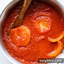 Lightened Marcella Hazan-inspired tomato sauce simmering in a pot with a halved onion