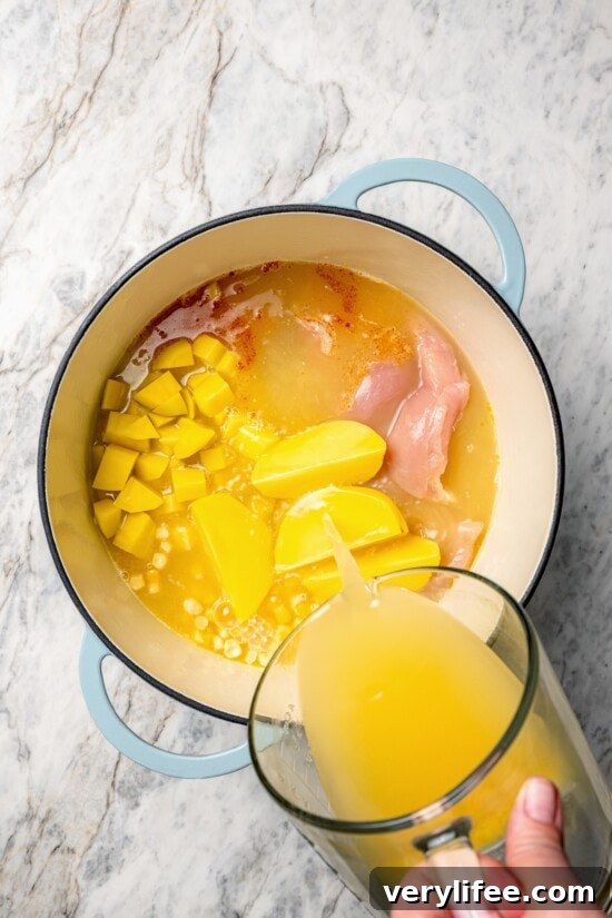Creamy Chicken and Corn Chowder Recipe 7 Pouring broth into dutch oven for chicken corn chowder.