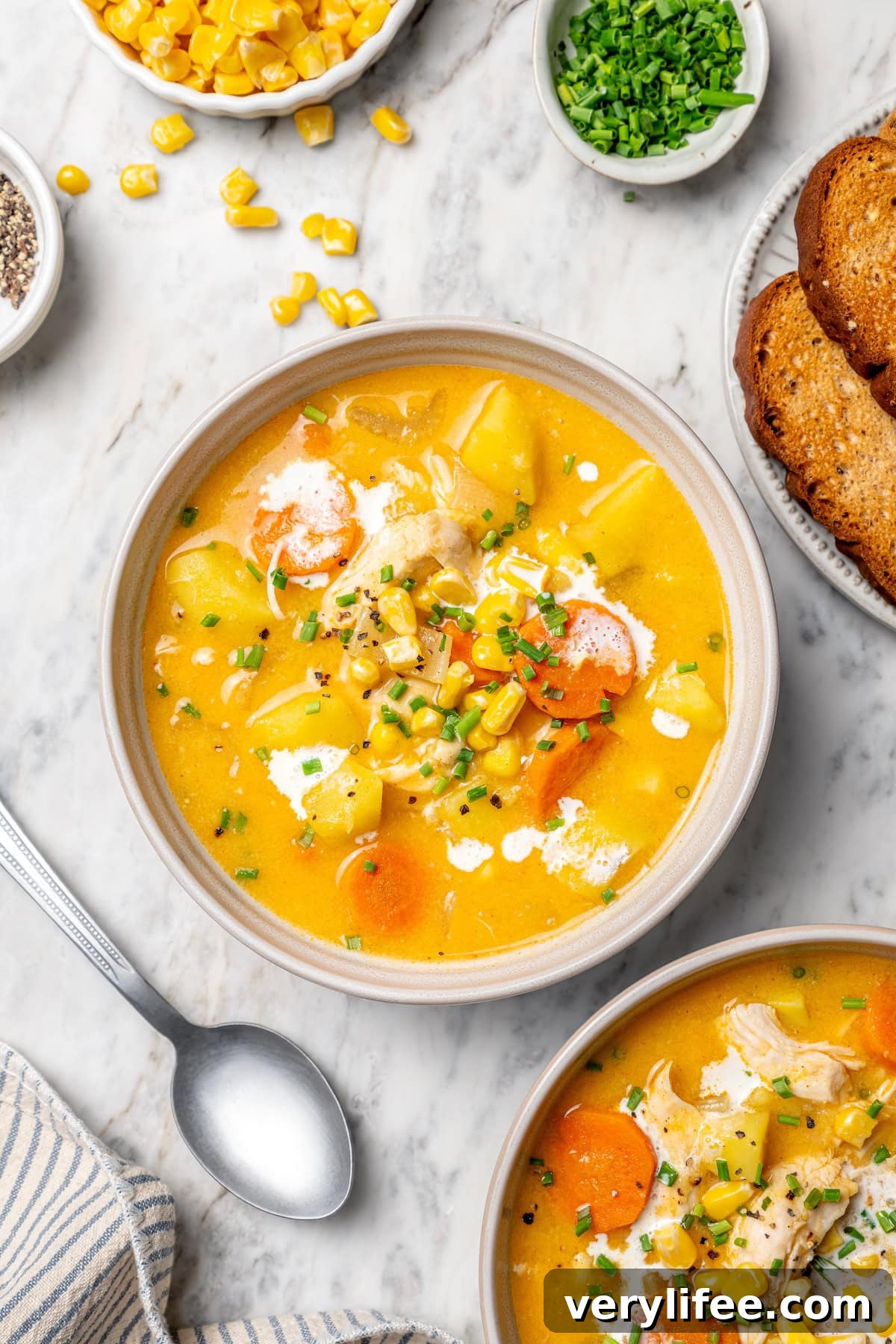 Creamy Chicken and Corn Chowder Recipe 9 Two bowls of creamy chicken corn chowder on marble tabletop.