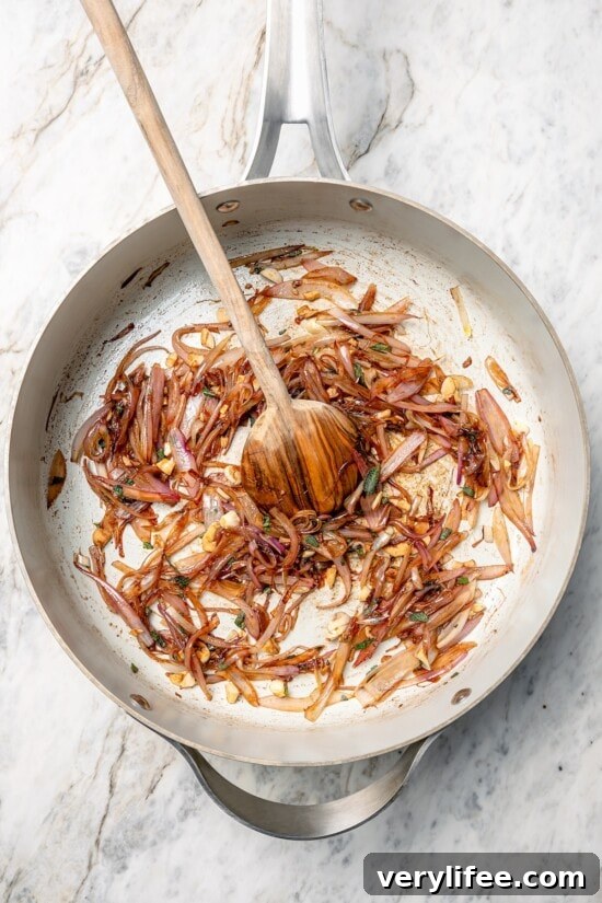 Shallots cooking in skillet with wooden spoon.