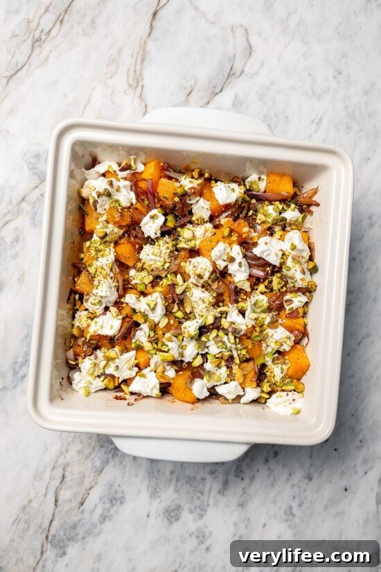Baked butternut squash in baking dish with goat cheese, pistachios, and shallots.