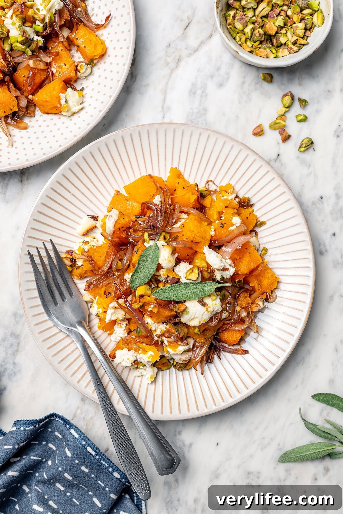 Baked butternut squash on 2 plates, topped with goat cheese, pistachios, shallots, and sage.