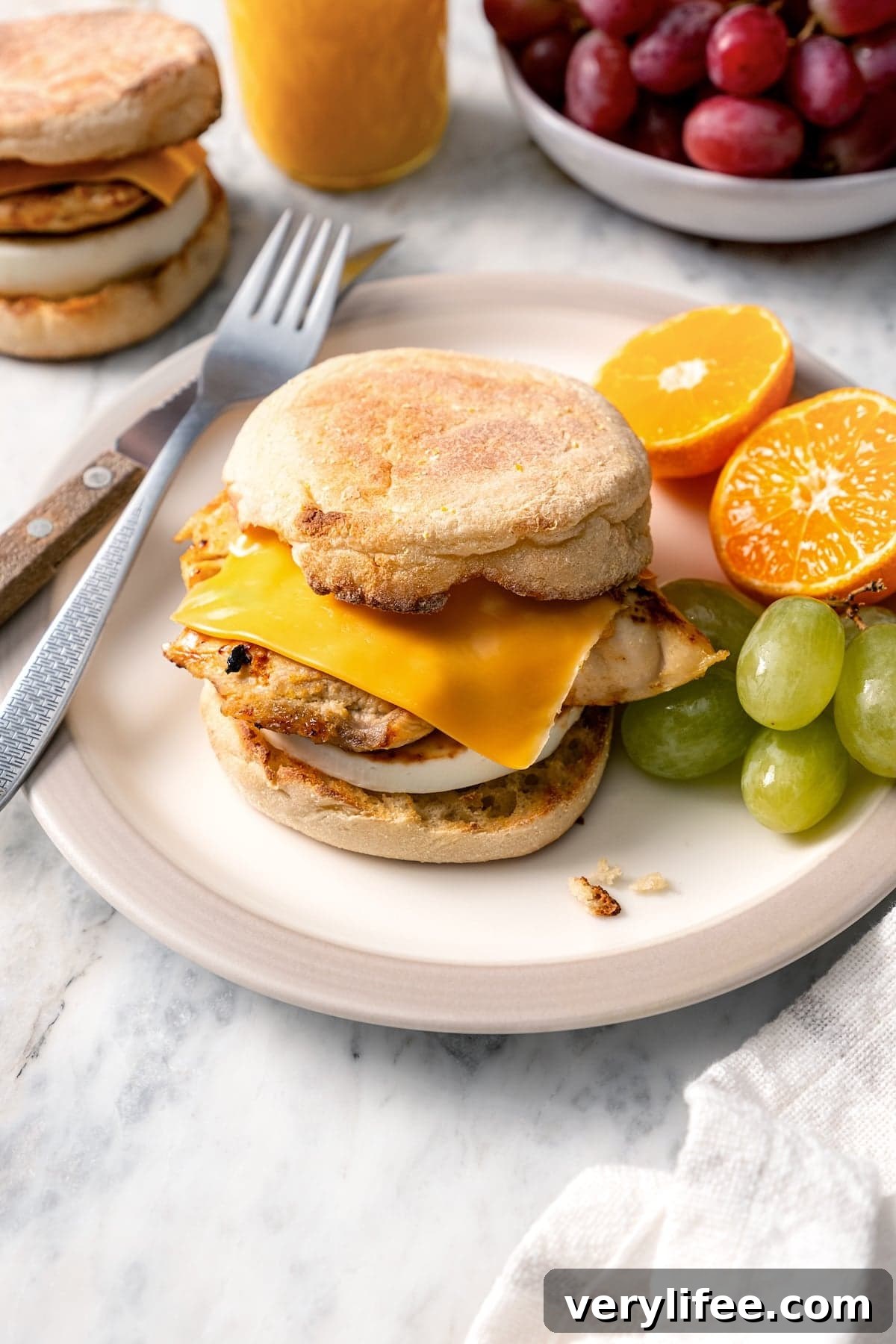 Copycat Chick-fil-A egg white grill sandwich on plate with grapes and orange halves.