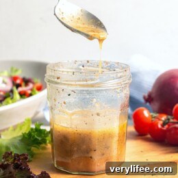 Greek salad dressing drizzling from spoon into jar.