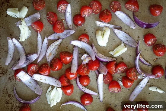 Sheet Pan Chicken with Roasted Tomatoes and Red Onions 2 garlic, red inions and tomatoes on a sheet pan.