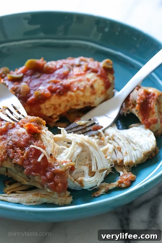 Partially shredded cooked salsa chicken on a blue plate next to two forks.