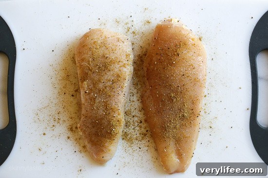Two seasoned chicken breasts side by side on a cutting board.