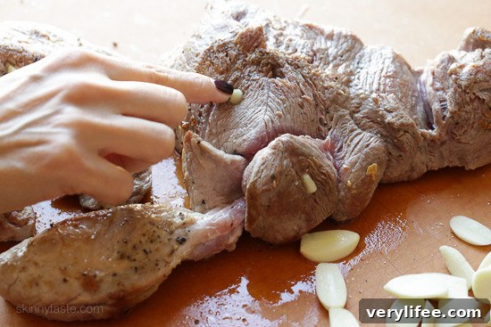 Instant Pot Carnitas: Authentic Mexican Pulled Pork 6 A hand presses garlic slivers into small holes cut in the side of a browned pork shoulder.