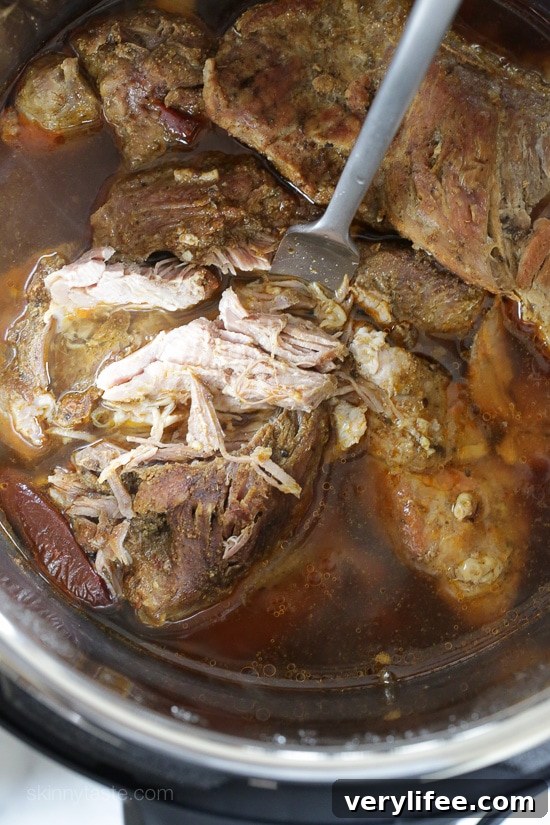 Instant Pot Carnitas: Authentic Mexican Pulled Pork 7 A fork stuck into cooked and partially shredded pork shoulder inside the Instant Pot.