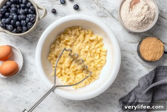 Moist Blueberry Banana Bread Recipe 4 Potato masher in bowl with mashed banana.