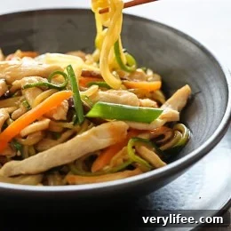 Chopsticks holding a zucchini noodle over a bowl of Chicken zoodle lo mein.