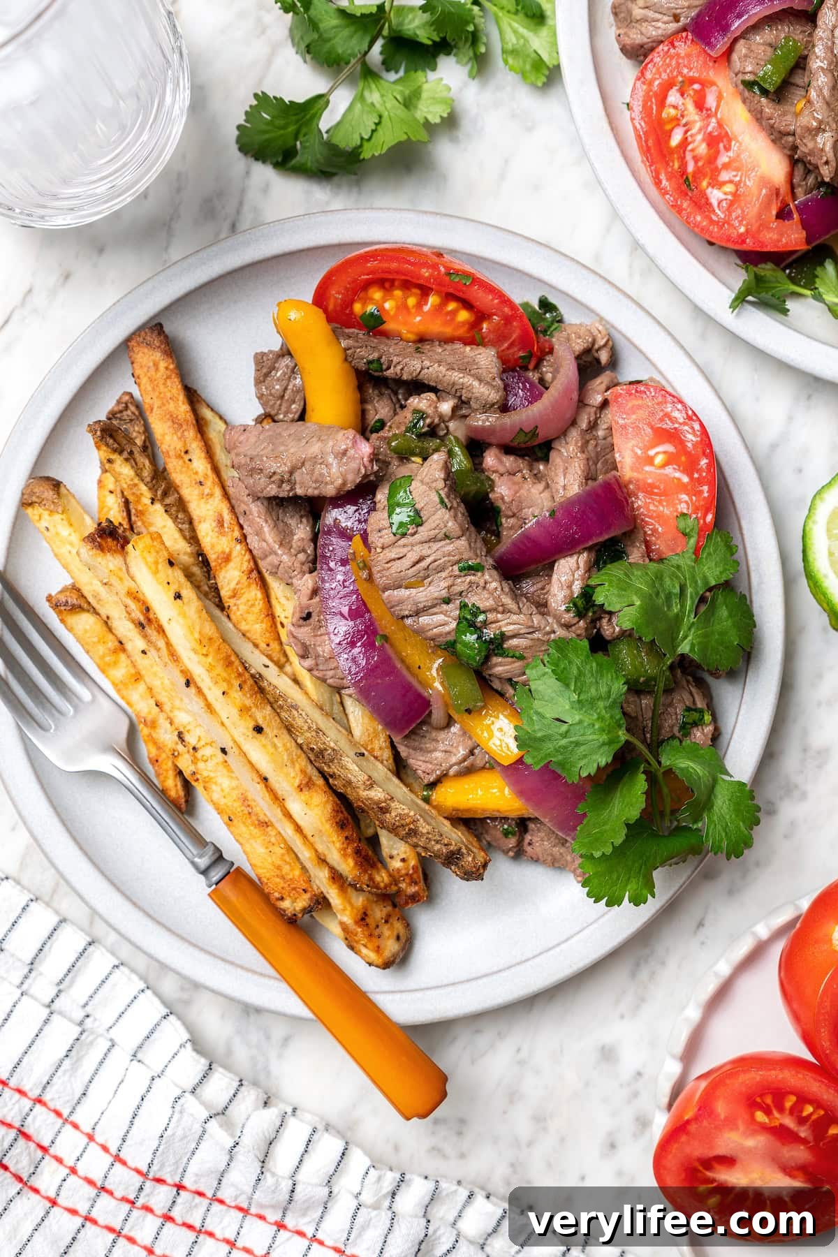 This lightened up Peruvian lomo saltado recipe is packed with flavor, with tender sirloin and veggies served alongside crispy baked fries. Peruvian lomo saltado on plate with fork and sprig of cilantro