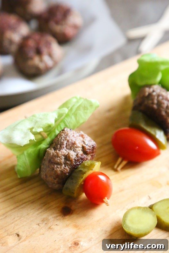 Mini burgers with bacon, layered on a bamboo skewer with lettuce, tomatoes and pickles