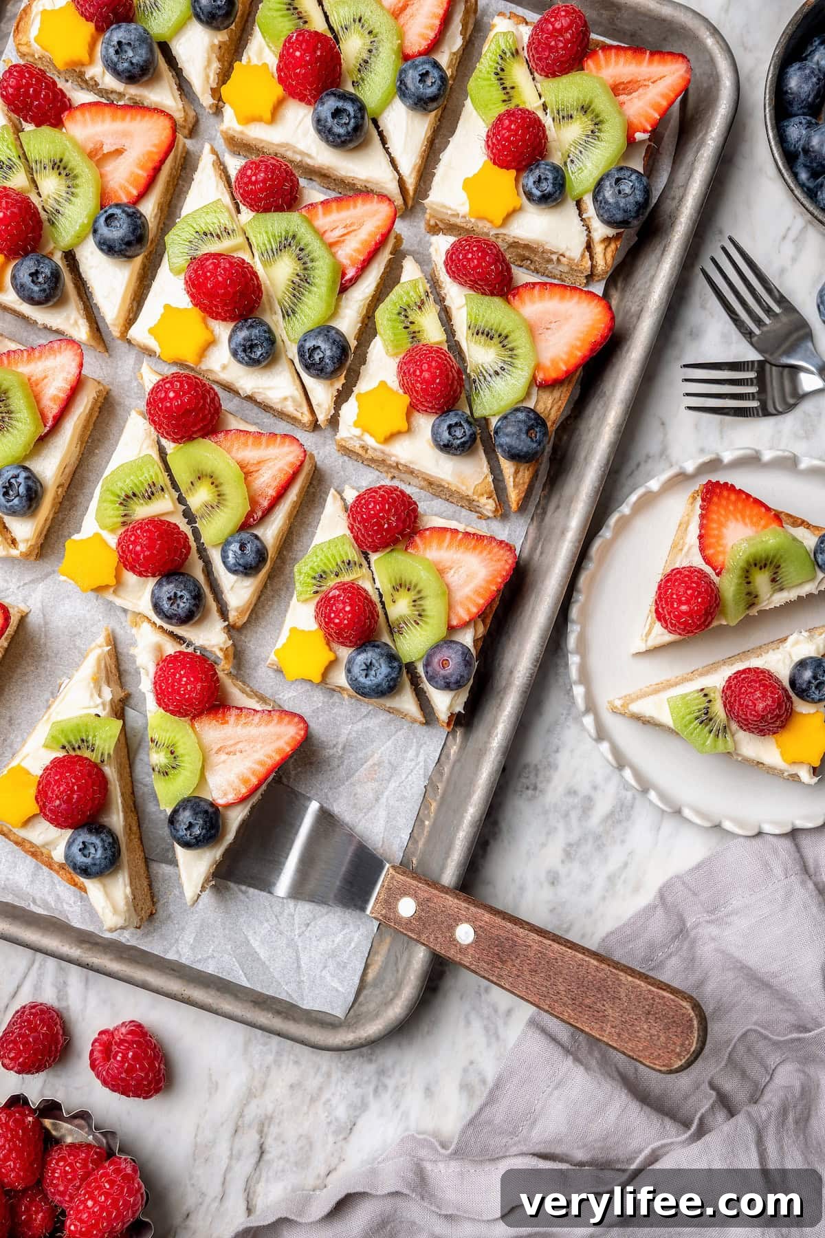 Overhead view of fruit pizza on sheet pan and plate