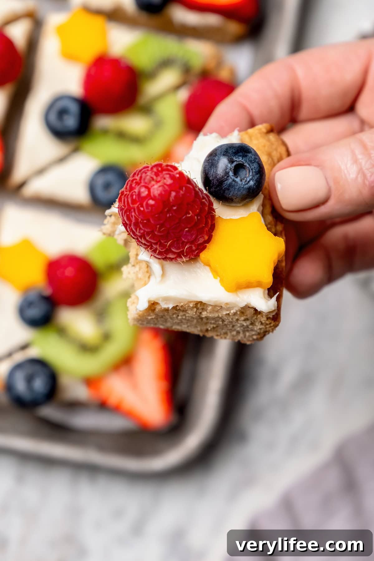 Hand holding piece of fruit pizza