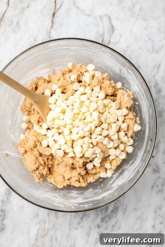 Overhead view of white chocolate chips being folded into bowl of dough