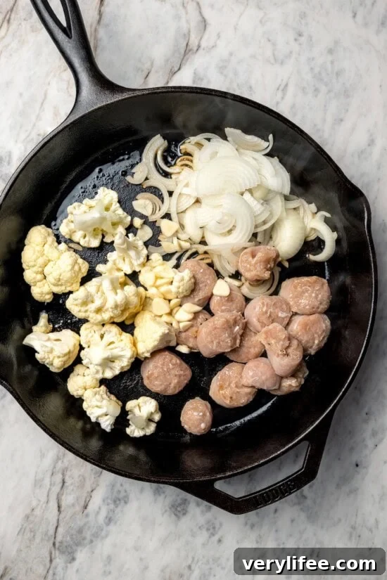 Low-Carb Chicken Scarpariello Recipe 7 Sausage, cauliflower, and onions added to cast iron skillet.