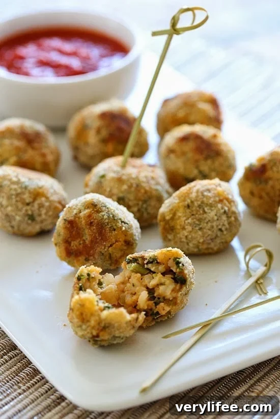 A plate of baked arancini rice balls with a dish of marinara sauce