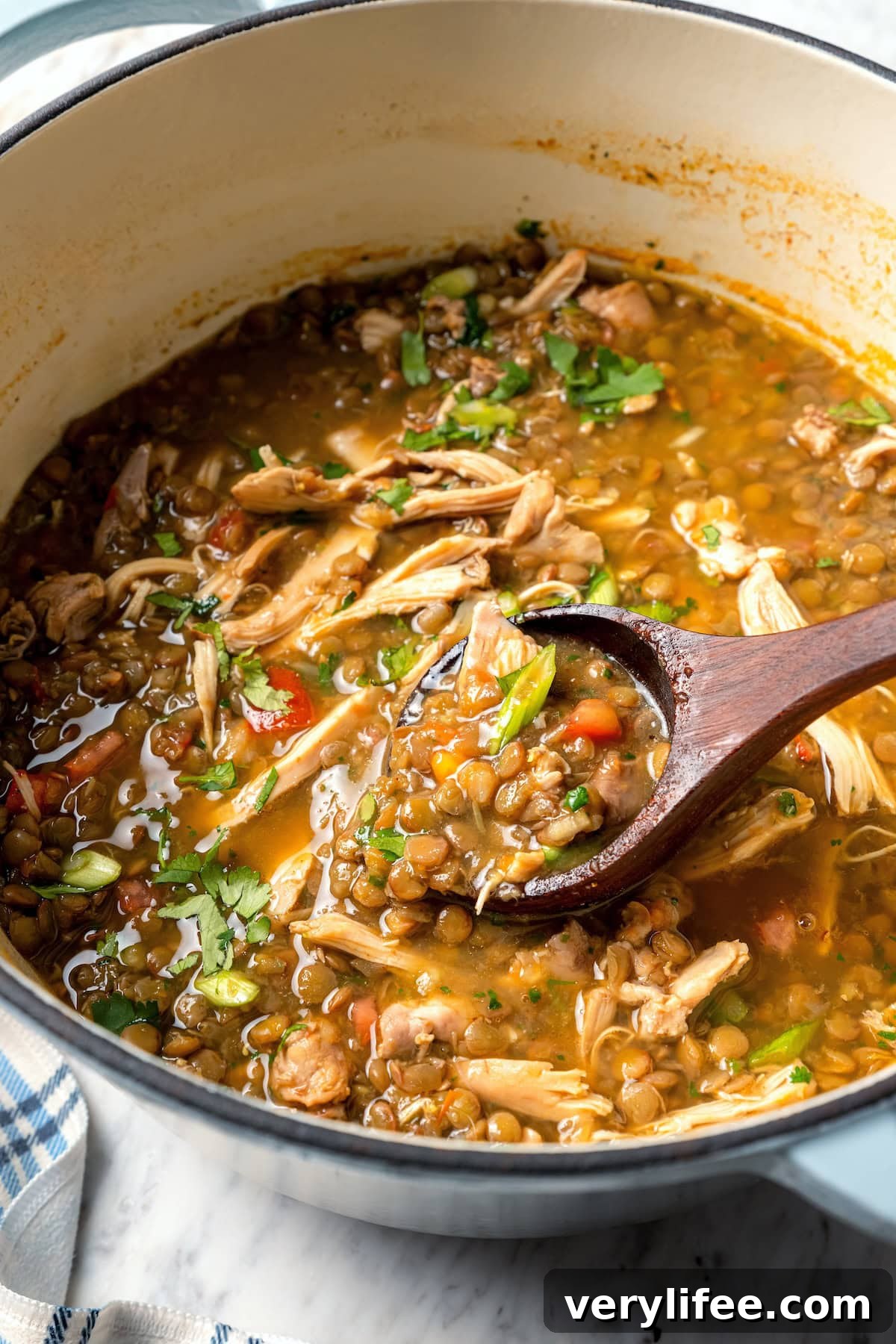 This chicken lentil soup is hearty, flavorful, and easy to make. It’s a nourishing, protein-packed meal perfect for cold days. Ladling chicken lentil soup from Dutch oven.