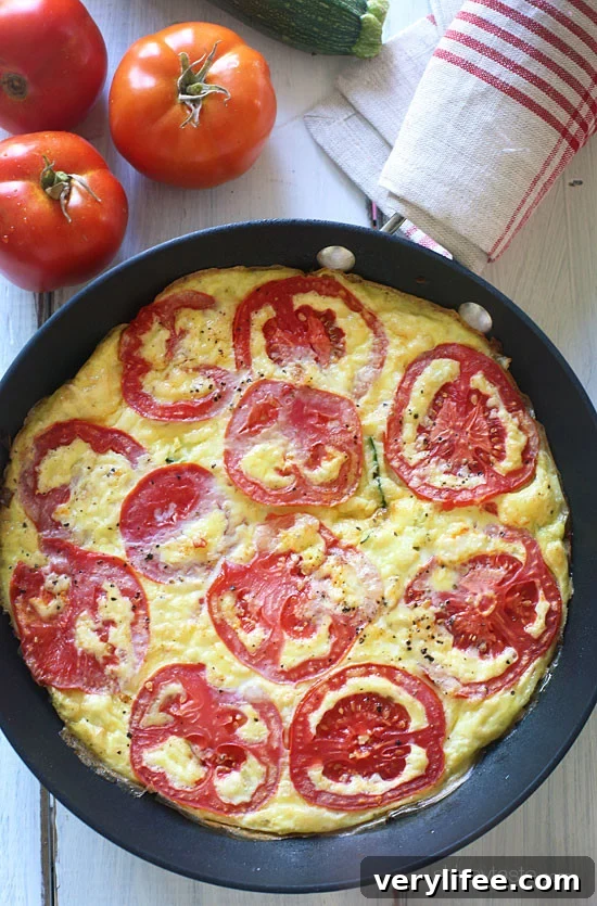 Tomato and Zucchini Frittata Recipe 5 Frittata in a skillet with sliced tomatoes on top.