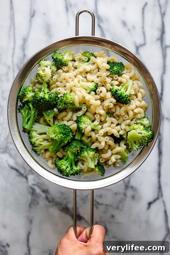 Creamy Broccoli Mac and Cheese Recipe 5 Hand holding colander with elbow noodles and broccoli.