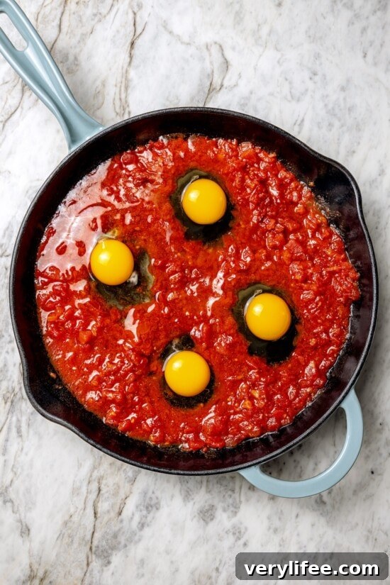 Add the eggs Eggs cracked into tomato sauce in skillet
