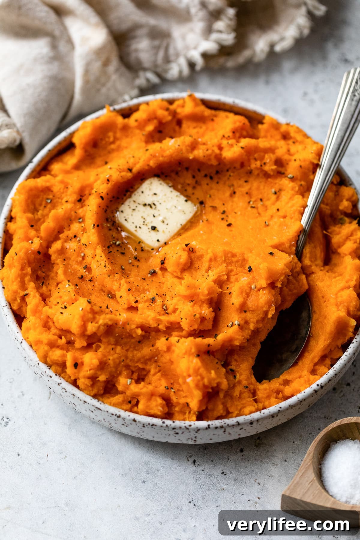 Mashed sweet potatoes topped with a pat of butter in a bow with a spoon.