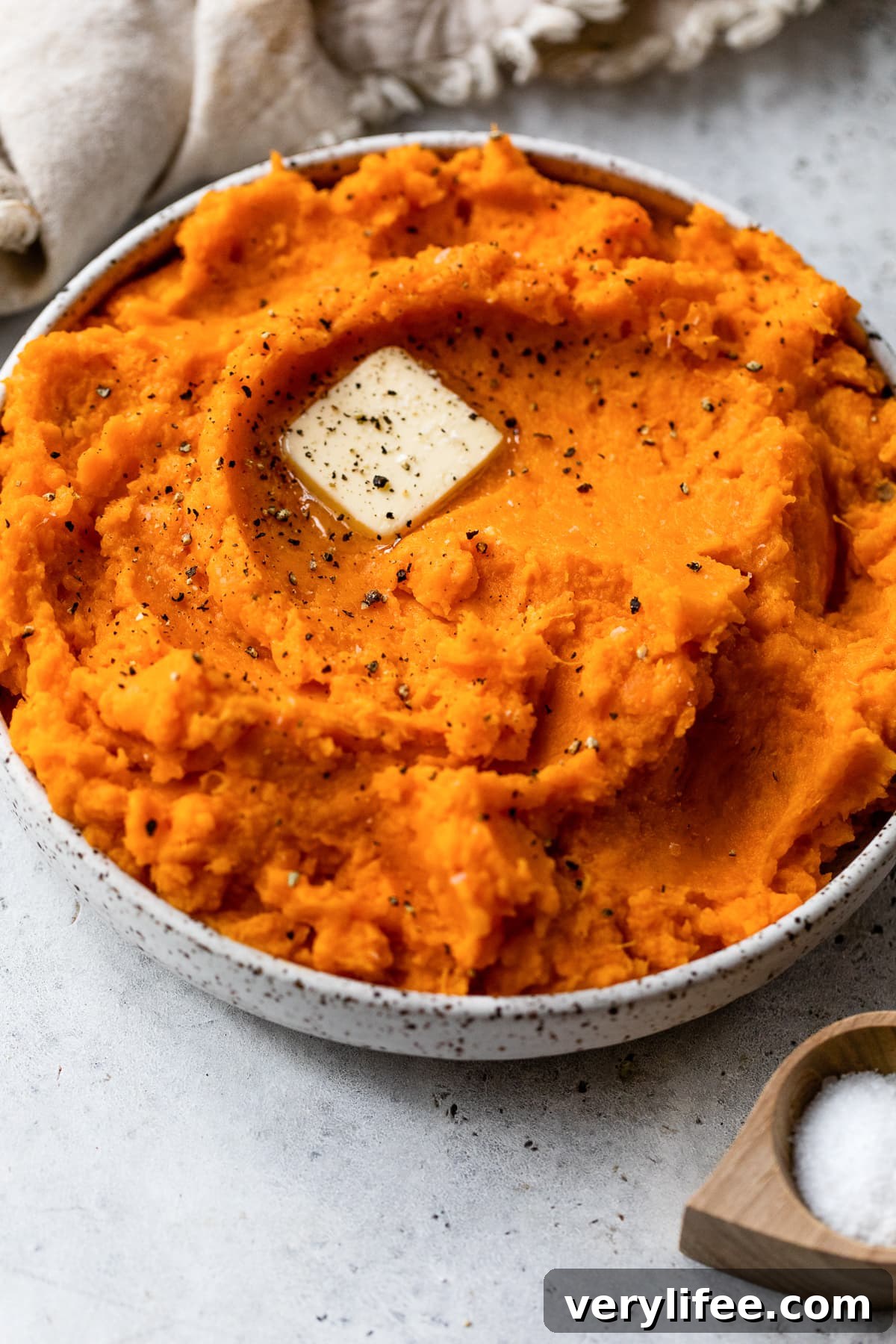 Mashed sweet potatoes topped with a pat of butter in a bowl with a spoon.