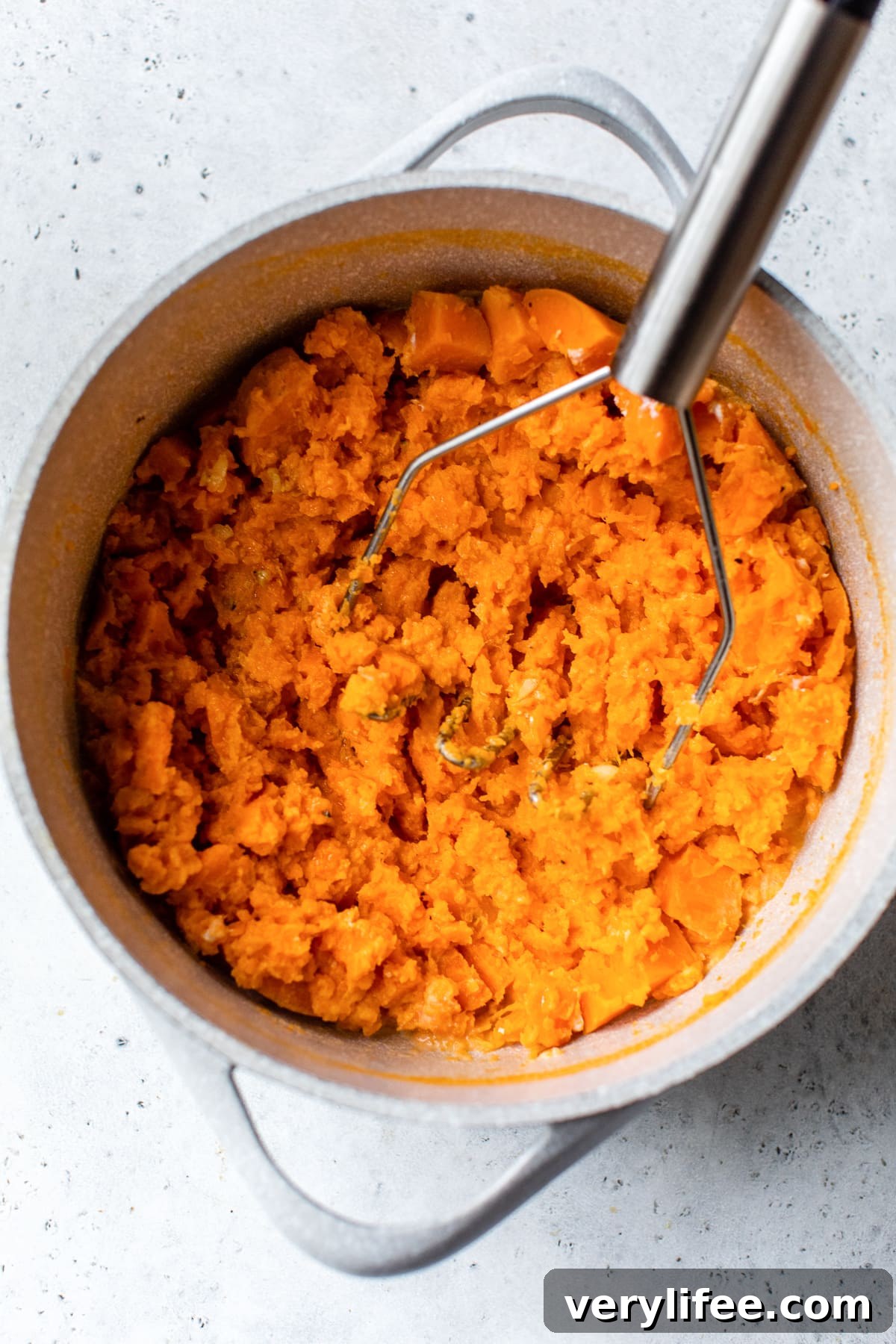 Sweet potatoes being mashed in a pot.