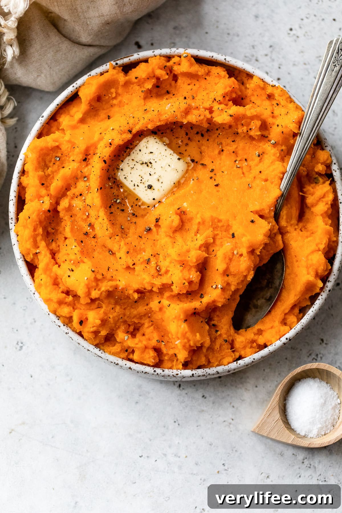 Overhead view of mashed sweet potatoes topped with a pat of butter in a bowl with a spoon.
