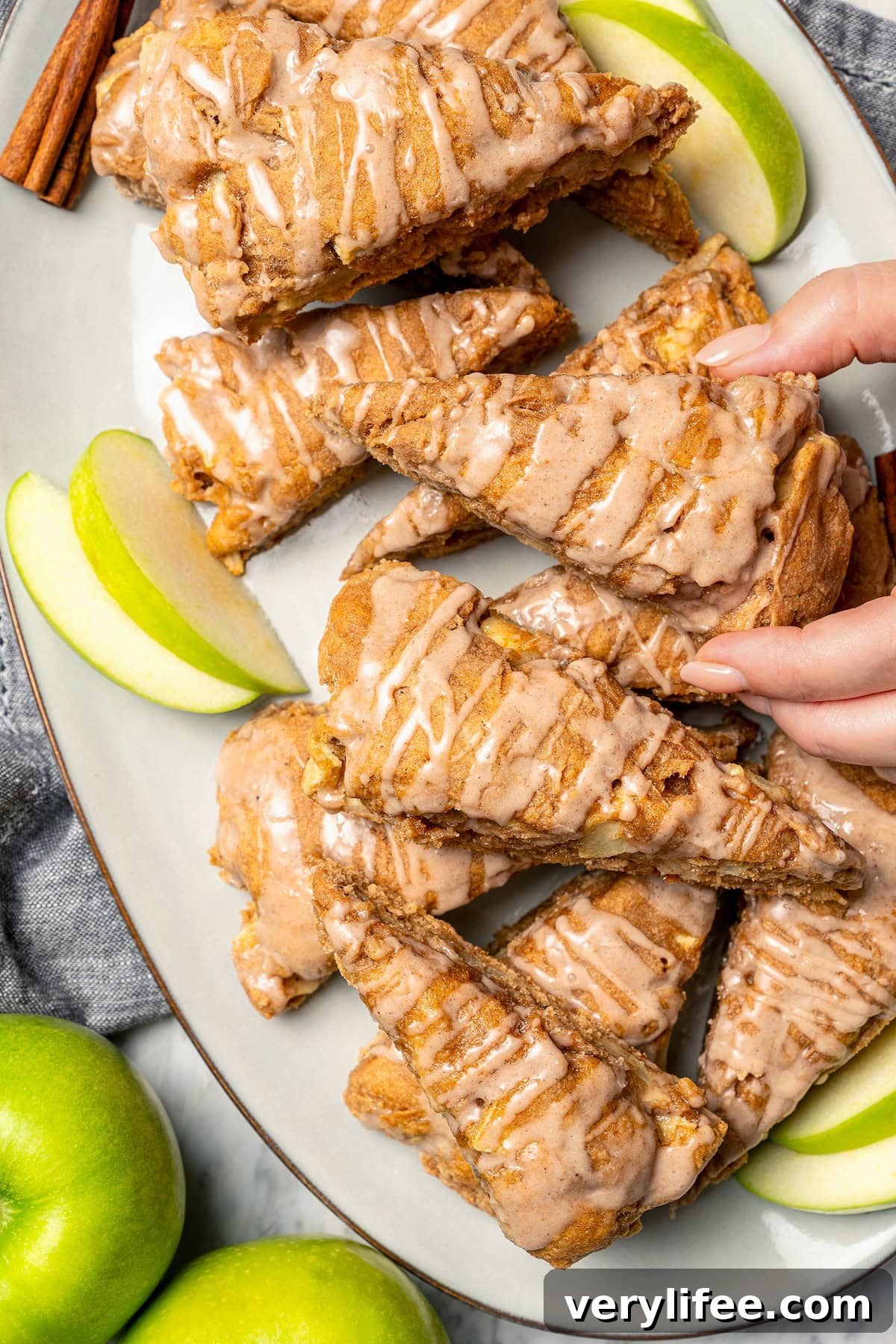 Hand grabbing glazed apple scone from platter