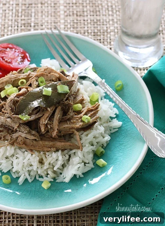 Slow cooked adobo pulled pork in a bowl, garnished with scallions