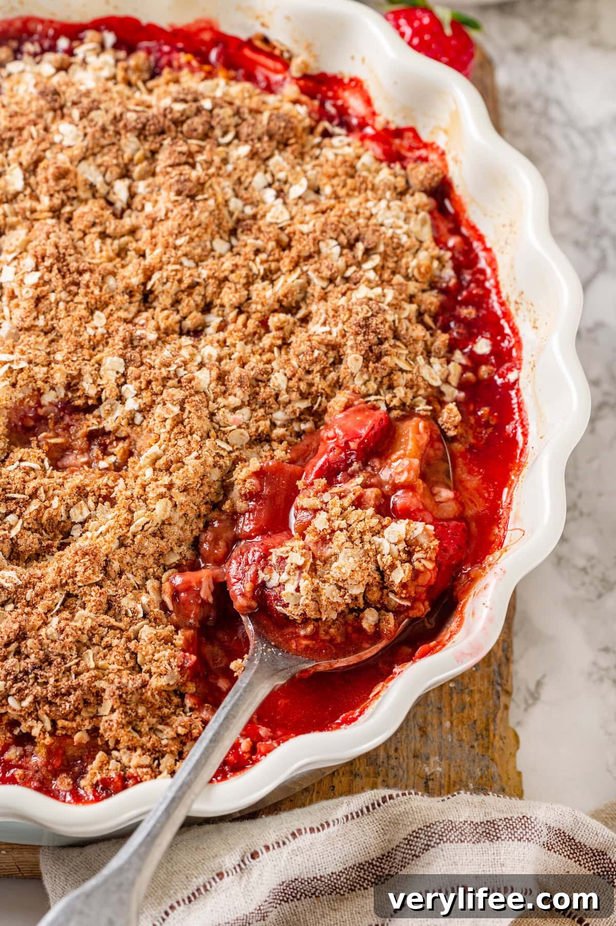 Honey adds the perfect amount of sweetness to the filling in this strawberry rhubarb crisp recipe. Easy to make and impossible to resist! Baking dish with strawberry rhubarb crisp with spoon scooping out serving