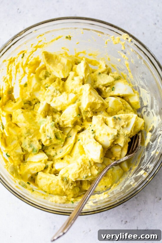Mixing ingredients for avocado egg salad sandwich in a bowl.