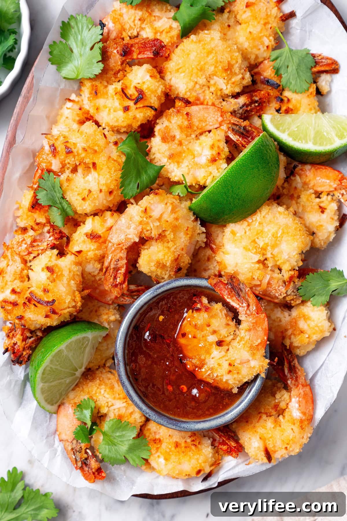 Platter of baked coconut shrimp, with one shrimp dipped into cup of sauce.