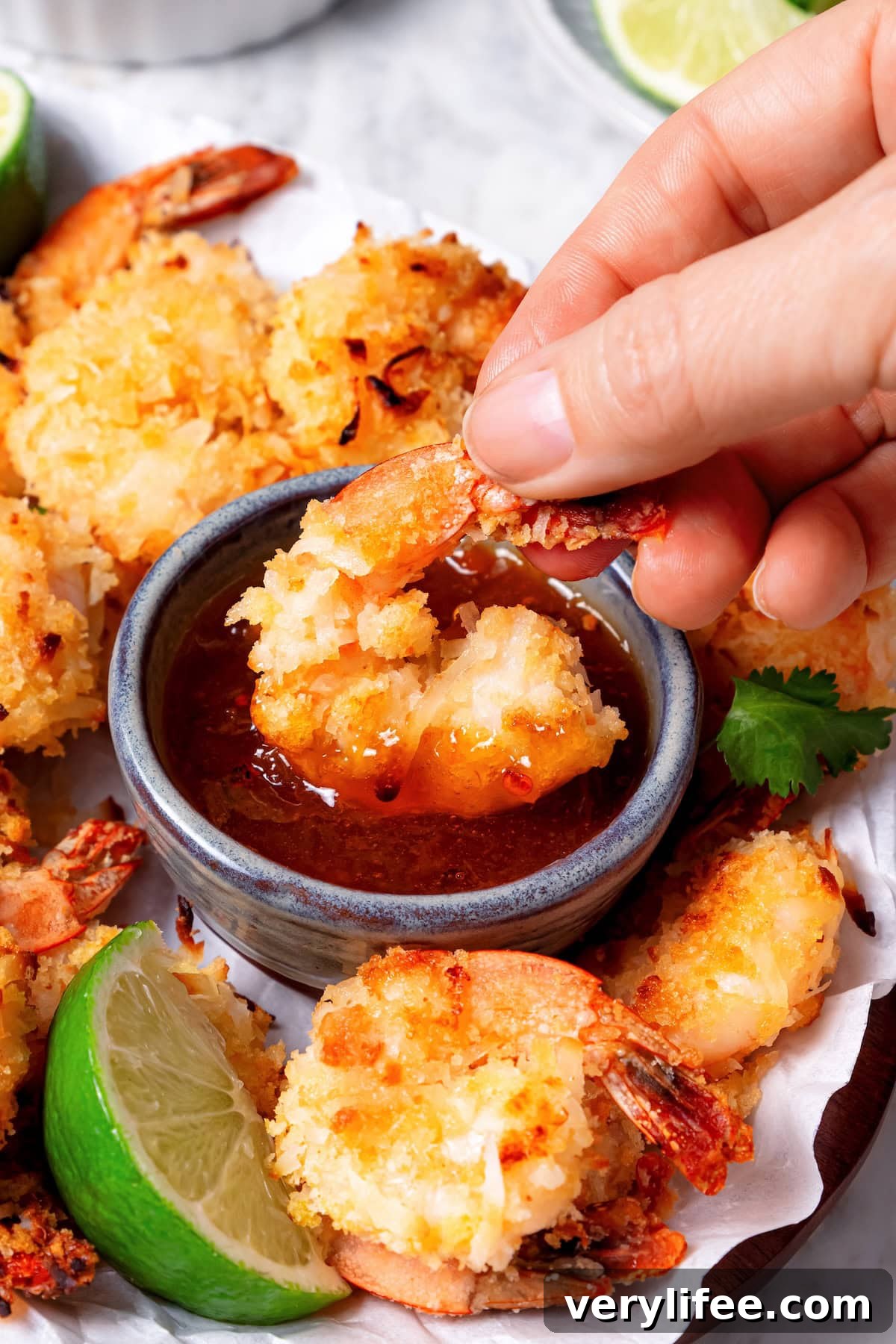 Hand dipping baked coconut shrimp into sauce.